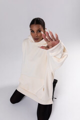 Wall Mural - Attractive african american woman in oversized white hoodie sits on white background.
