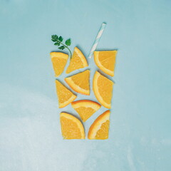 minimal flatlay creative composition of glass of orange slice with green natural leaf and straw on bright blue background.