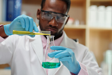 Wall Mural - Laboratory worker in protective glasses mixing green and yellow liquids