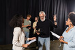 © LIGHTFIELD STUDIOS - bearded art director pointing with finger while reading screenplay near multiethnic actresses during acting skills lesson.