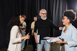 © LIGHTFIELD STUDIOS - cheerful african american woman holding screenplay and laughing near bearded producer and multiethnic actors in theater.
