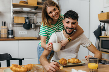 Wall Mural - Happy couple in the kitchen, looking at the camera, breakfast time