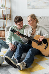 Wall Mural - cheerful blonde woman playing acoustic guitar near curly boyfriend.