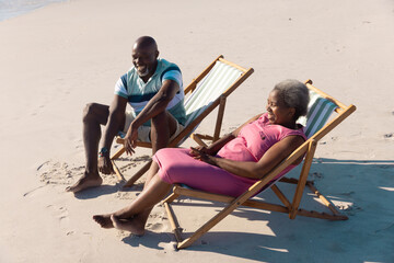 High angle view of happy african american senior couple sitting on deckchairs and talking at beach