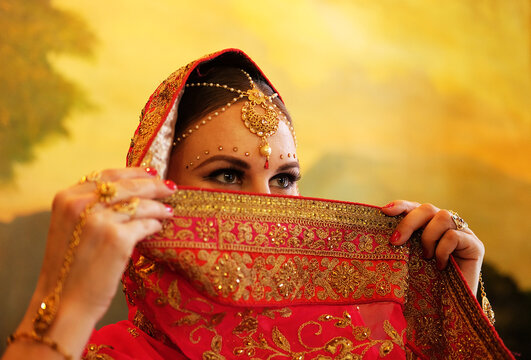 Young hindu woman model with traditional jewelry. Indian costume red saree. Indian or Muslim woman covers her face.