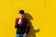 © Cavan Images - Young teen leaning against a yellow wall while using a mobile phone
