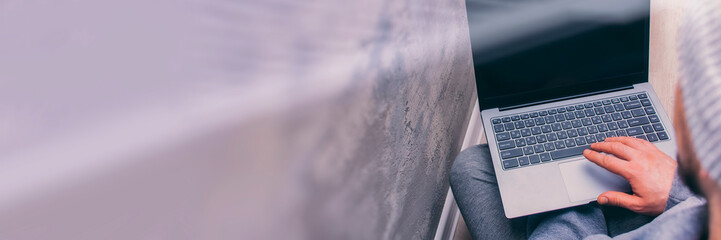 Man in gray clothes sits with a laptop against a concrete wall. Freelancer's loft interior.