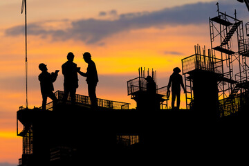 Silhouette of Engineer and worker checking project at building site background, construction site at sunset in evening time