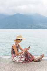 Canvas Print - woman with hat sit at a pier using cellphone