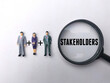 Miniature people and magnifying glass with the word STAKEHOLDER.