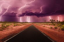 Deserted Australian Outback Landscape With Red Dirt Road Towards Horizon With Bushes In Roadsides And Heavy Thunderstorm With White Purple Lightnings On The Horizon. Generative AI