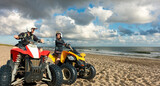Fototapeta Sawanna - Quad driving people - happy smiling couple bikers in sand beach. North Sea, Denmark.