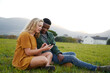 © StratfordProductions - Young multiracial couple sitting and talking while using mobile phone in field
