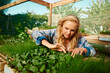 © StratfordProductions - Young caucasian woman looking down and examining plants in plant nursery