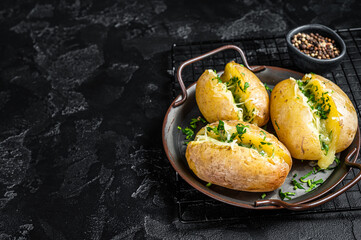 Wall Mural - Baked Jacket potatoes with cheese, herbs and butter. Black background. Top view. Copy space