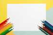 © OneClic - White paper sheet with colored pencils on kid desk. Top view of blank background for drawing. Colorful shcool activity background.