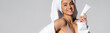 © LIGHTFIELD STUDIOS - Cheerful young woman with towel on head holding cosmetic lotion isolated on grey, banner.