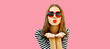 Portrait of beautiful young woman blowing her lips with lipstick sending sweet air kiss wearing red heart shaped sunglasses on pink background