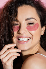 Wall Mural - Portrait of curly young woman with eye patches looking at camera on pink background.