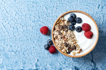 Wall Mural - Yogurt with berries and muesli for breakfast in bowl on bue background. Top view. Copy space