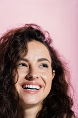 Wall Mural - Portrait of freckled and curly woman looking away isolated on pink.