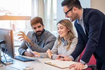 Smart young male leader supervisor reviewing online sales report on computer, working with motivated colleagues. Concentrated three millennial employees preparing presentation in modern office.