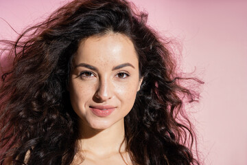 Wall Mural - Freckled brunette woman smiling at camera on pink background.