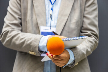 Journalist correspondent or reporter at media event, holding microphone, writing notes. Journalism concept.