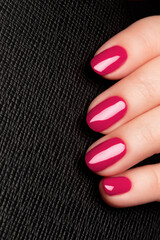 Wall Mural - Female hand with beautiful manicure - viva magenta, pink nails on black leather surface background. Nail care concept