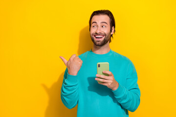 Wall Mural - Photo of young excited gadget progressive user man enjoy technology hold smartphone finger point empty space isolated on yellow color background