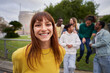 © CarlosBarquero - Portrait of a Young red-haired girl with wide smile and piercing look at the camera. Group of friends gathered in the background of the image. Colleagues hanging out in the city. Outdoors.