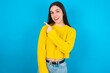 © Jihan - young brunette girl wearing yellow knitted sweater against blue wall glad cheery demonstrating copy space look novelty