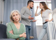 © JackF - Portrait of sad mature woman sitting at home ignoring conflict of young couple arguing, figuring out relations at home