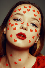 Wall Mural - Portrait of a woman with stickers of hearts on her face. Fashion photo of artistic professional makeup, woman with red lips on gray background. Love and feelings, style February 14, Valentine's Day.