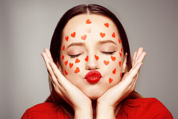 Wall Mural - Portrait of a woman with stickers of hearts on her face. The girl blows an air kiss on the camera, on a gray background. Self-love, skin care, makeup, courses for women, dating.