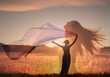 © kieferpix - woman in the field feeling free at peace in nature holding fabric cloth blowing in the wind.