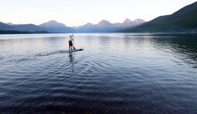 A Man Stand Up Paddle Boards (SUP) On A Calm Lake McDonald In Glacier National Park.