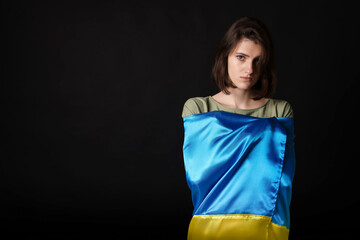 Poster - Sad woman wrapped in Ukrainian flag on black background. Space for text