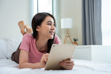 Wall Mural - Asian attractive woman using tablet chat on bed at home in the morning. 