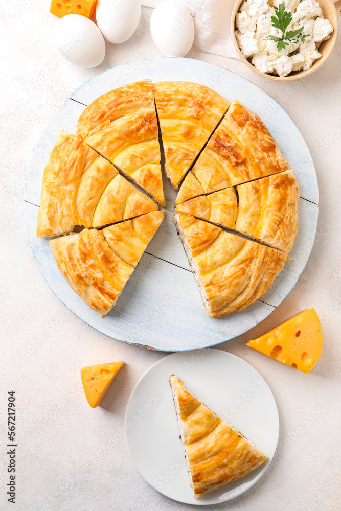 Board and plate with pieces of delicious cheese pie on white table
