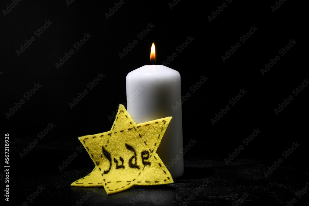 Burning candle and Jewish badge on dark background. International Holocaust Remembrance Day