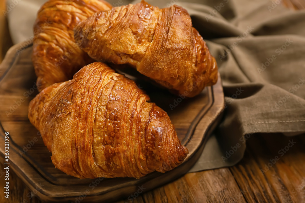 Board with delicious croissants on wooden background, closeup