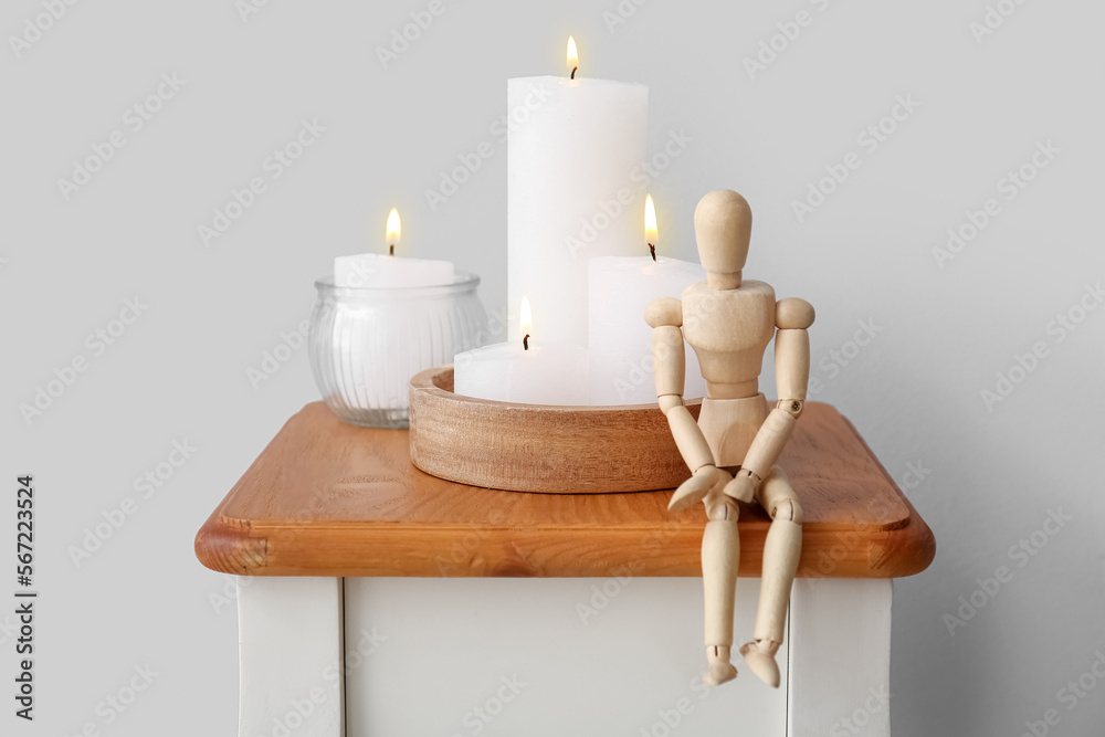 Burning candles and wooden mannequin on end table near grey wall
