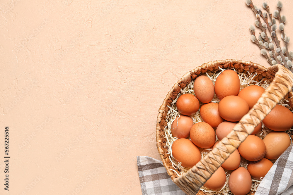 Wicker basket with Easter eggs and pussy willow branches on beige background