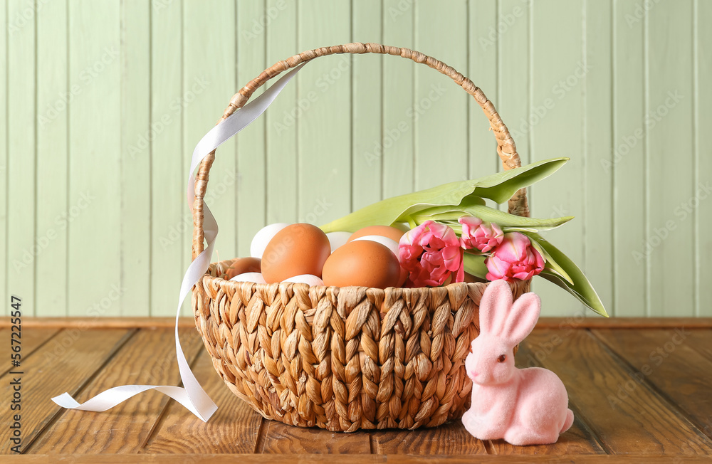 Wicker basket with Easter eggs, tulip flowers and pink bunny on wooden table