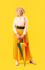 Wall Mural - Beautiful mature woman with rainbow umbrella on yellow background