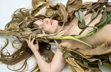 Fashion Portrait Of Young Sexy Nude Brunette Woman, Artfully Covered With Dry, Withered Decorative Brown Banana Leaves