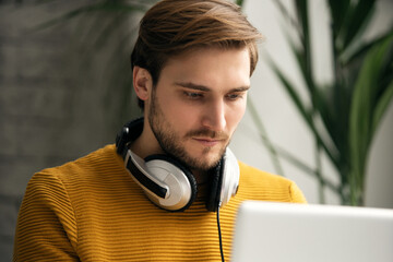 Wall Mural - Casually dressed young designer listening music on headphones while working on a laptop in an office