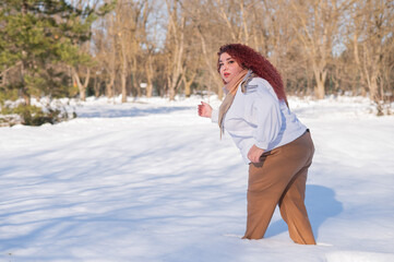 A fat red-haired woman in a white sweatshirt walks through snowdrifts. 