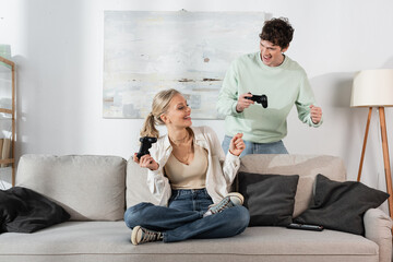 Wall Mural - KYIV, UKRAINE - OCTOBER 24, 2022: joyful young couple holding joysticks while playing video game 